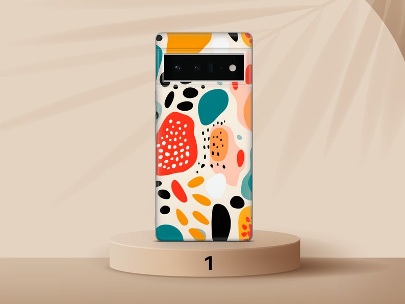 以下が含まれることがあります： カラフルな抽象的なデザインが施された白い携帯電話ケース。デザインには、赤、オレンジ、黄色、緑、青、黒など、さまざまな形と色が含まれています。