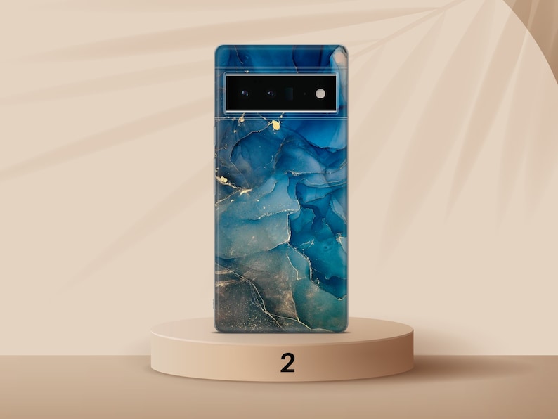 May include: A blue and gold abstract phone case with a camera cutout. The case is on a light brown pedestal with the number "2" printed on it.