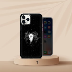 K&ouml;nnte beinhalten: Schwarze Handyh&uuml;lle mit wei&szlig;em Widder-Sch&auml;del-Design. Die H&uuml;lle hat einen gesprenkelten Hintergrund und eine detaillierte Illustration eines Widder-Sch&auml;dels mit H&ouml;rnern und einem Pentagramm-Symbol. Die Handyh&uuml;lle wird auf einem beigen Podest pr&auml;sentiert.