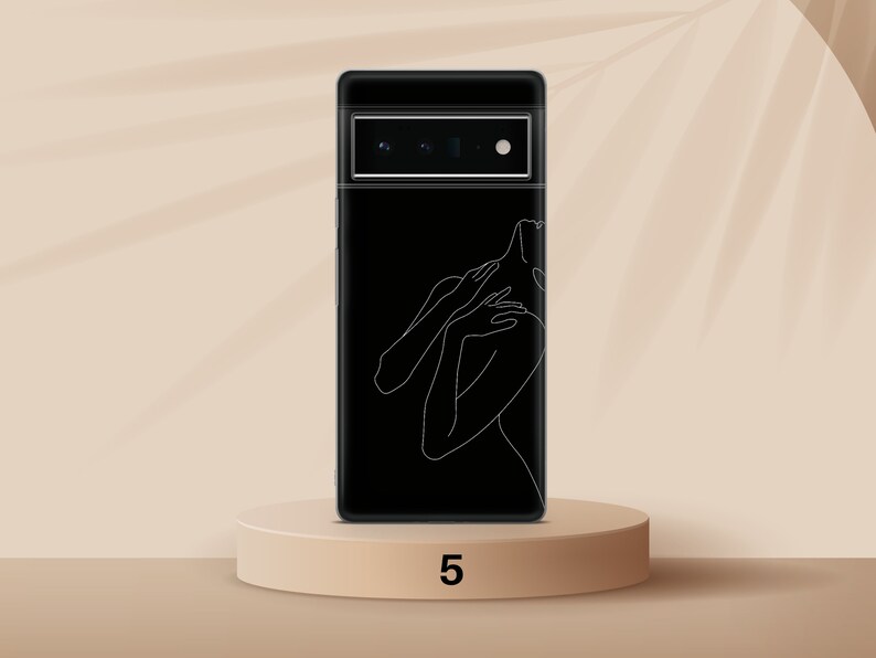 Puede incluir: Una funda de tel&eacute;fono negra con un dibujo de l&iacute;nea blanca de una persona. La funda de tel&eacute;fono est&aacute; en una plataforma beige con el n&uacute;mero 5 impreso en ella.