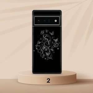 Puede incluir: Una funda de tel&eacute;fono negra con un dibujo de l&iacute;nea blanca de una cara rodeada de mariposas y planetas. La funda tiene un fondo negro y un recorte para el objetivo de la c&aacute;mara.