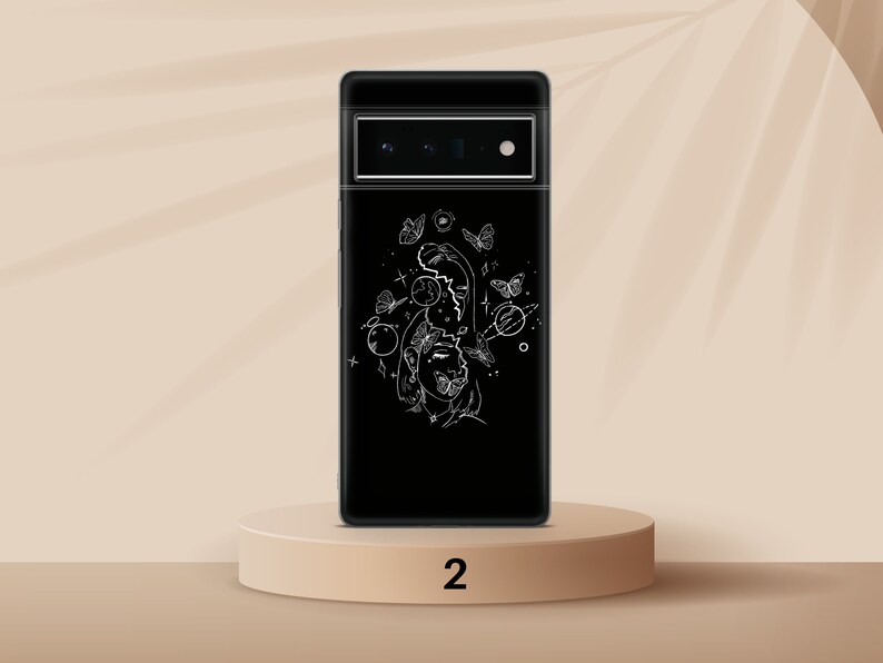 Puede incluir: Una funda de tel&eacute;fono negra con un dibujo de l&iacute;nea blanca de una cara rodeada de mariposas y planetas. La funda tiene un fondo negro y un recorte para el objetivo de la c&aacute;mara.