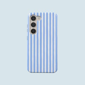 Puede incluir: Funda de teléfono con un patrón de rayas verticales en azul claro y blanco. La funda tiene un módulo de cámara con tres lentes y un flash. El fondo es azul claro liso.