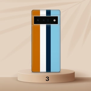 K&ouml;nnte beinhalten: Ein Smartphone mit einer blauen, wei&szlig;en, orangen und schwarzen gestreiften H&uuml;lle. Das Telefon befindet sich auf einem hellbraunen Sockel mit der Nummer "3" darauf.