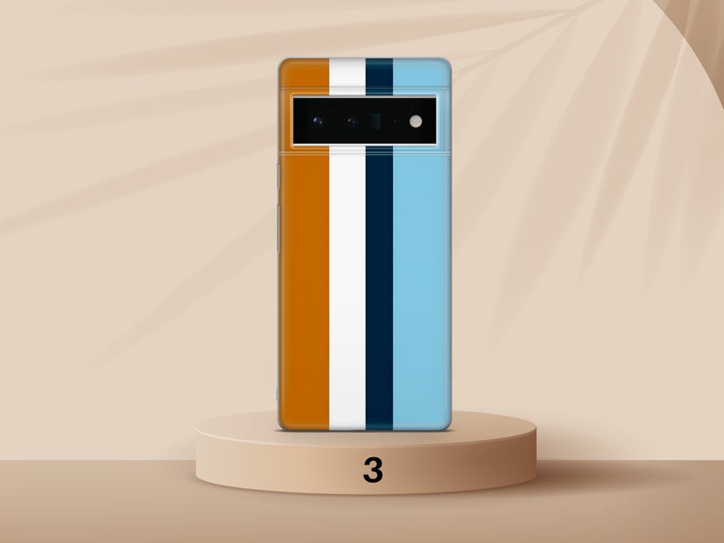 K&ouml;nnte beinhalten: Ein Smartphone mit einer blauen, wei&szlig;en, orangen und schwarzen gestreiften H&uuml;lle. Das Telefon befindet sich auf einem hellbraunen Sockel mit der Nummer "3" darauf.