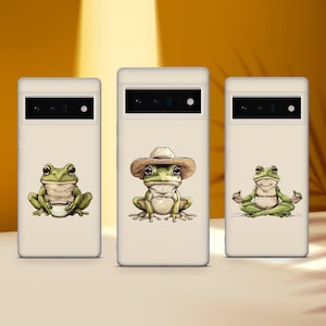 May include: Three white phone cases with different frog illustrations. The first case features a frog holding a cup of coffee. The second case features a frog wearing a cowboy hat. The third case features a frog sitting in a yoga pose.