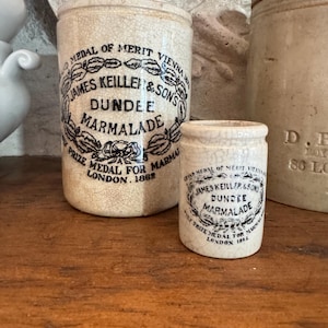 May include: Two antique Dundee Marmalade jars. The jars are off-white with black text and a decorative emblem. The text reads "James Keiller & Sons Dundee Marmalade" and "Prize Medal for London 1862".