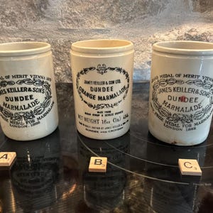 May include: Three off-white ceramic marmalade jars with black printed text and decorative borders. Each jar features the James Keiller & Son Ltd Dundee Orange Marmalade branding, including references to the 1873 Vienna and 1862 London prize medals.