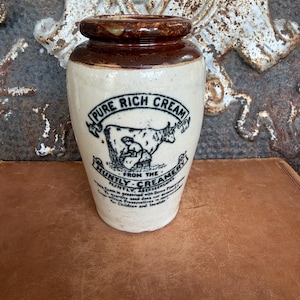 Peut inclure: Un pot en céramique de couleur crème avec un bord émaillé brun foncé. L'avant présente un texte noir indiquant PURE RICH CREAM FROM THE HUNTLY CREAMERY, HUNTLY, ABERDEENSHIRE, ainsi qu'une illustration d'une vache et d'une personne.