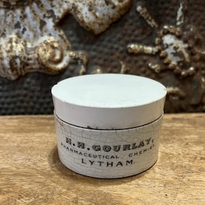 May include: A white ceramic jar with a cracked glaze. The jar has black lettering that reads "H.H. GOURLAY, PHARMACEUTICAL CHEMIST, LYTHAM."