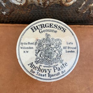 May include: A set of three ceramic mugs with a speckled, cream-colored glaze. Each mug features a different hand-painted design: a blue and green leaf, a yellow flower, and a red berry. The mugs have a simple, rounded shape.