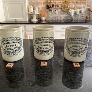 May include: Three off-white ceramic marmalade jars with black printed text reading James Keiller & Sons Dundee Marmalade, Grand Medal of Merit Vienna 1873, and Prize Medal for Marmalade London 1862. Each jar is labeled with a small wooden letter tile A, B, or C.