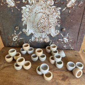 May include: A collection of small, handmade ceramic pots in various shades of beige and white. The pots are stacked in groups of three, creating a visually appealing display.