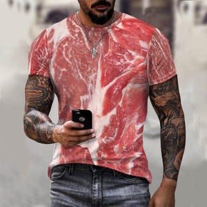 Può includere: Una maglietta a maniche corte con una stampa rossa e bianca di un pezzo di carne cruda.