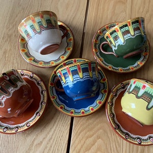 Könnte beinhalten: Set aus fünf bunten Keramik-Kaffeetassen und Untertassen mit aufwendigen bemalten Designs. Jede Tasse und Untertasse hat eine andere Farbe und ein anderes Muster, darunter Blau, Grün, Gelb, Braun und Weiß.