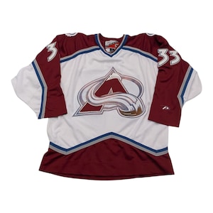 May include: White hockey jersey with maroon and blue accents. The jersey features the Colorado Avalanche logo with the number 33 on the right sleeve.