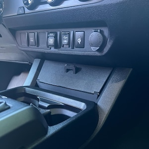 May include: A close-up of a car's dashboard, featuring various buttons, dials, and a small storage compartment. The dashboard is primarily black, with silver accents on the dials. There are buttons labeled "ECT PWR" and "REAR".
