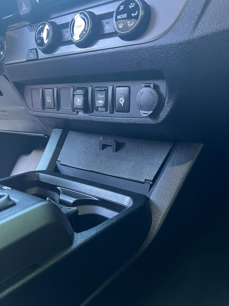 May include: A close-up of a car's dashboard, featuring various buttons, dials, and a small storage compartment. The dashboard is primarily black, with silver accents on the dials. There are buttons labeled "ECT PWR" and "REAR".