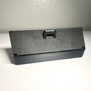 May include: A black rectangular object with a textured surface and a small handle. The object has a matte finish and is set against a white background.