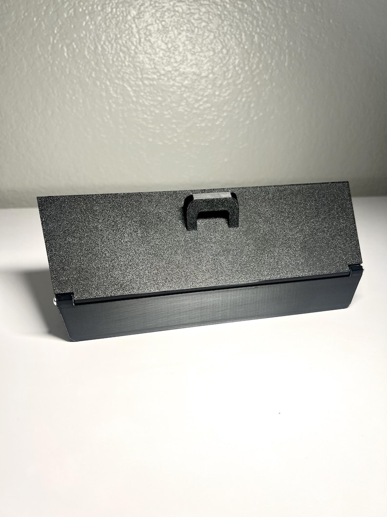 May include: A black rectangular object with a textured surface and a small handle. The object has a matte finish and is set against a white background.