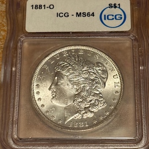 May include: A silver coin from 1881, encased in a clear plastic holder. The coin shows a profile of a woman and the text "LIBERTY" and "UNITED STATES OF AMERICA". The holder is labelled "1881-O" and "ICG - MS64".