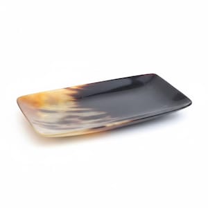 May include: A rectangular tray crafted from polished horn, featuring a smooth, glossy surface with a natural gradient of colors transitioning from deep black to translucent amber and cream tones, showcasing organic patterns and variations.