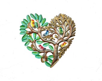 May include: A heart-shaped metal wall art piece featuring a tree with green leaves on the left side and textured brown branches on the right. Five small, colorful birds in yellow, blue, green, and red are perched among the branches.