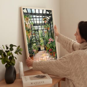 May include: A watercolour painting of a greenhouse interior with a variety of plants and flowers in pots. The greenhouse has a glass roof and metal frame. The painting is framed in a light wood frame.