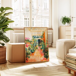 Puede incluir: Una impresi&oacute;n art&iacute;stica enmarcada que representa una colorida escena de invernadero con flores y plantas vibrantes en macetas de terracota. La obra de arte tiene una paleta de colores c&aacute;lidos con tonos naranja, rosa y verde. La impresi&oacute;n se muestra en un suelo de madera.