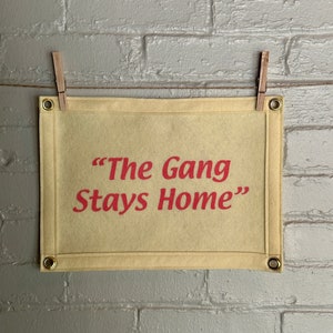 A cream felt banner with a phrase in bright pink ink reading "The Gang Stays Home" in the style of It's Always Sunny in Philadelphia.