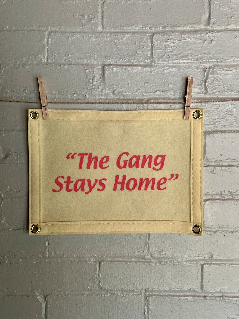 A cream felt banner with a phrase in bright pink ink reading "The Gang Stays Home" in the style of It's Always Sunny in Philadelphia.