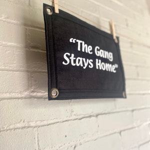 A black felt banner with a phrase in bright white ink reading "The Gang Stays Home" in the style of It's Always Sunny in Philadelphia.