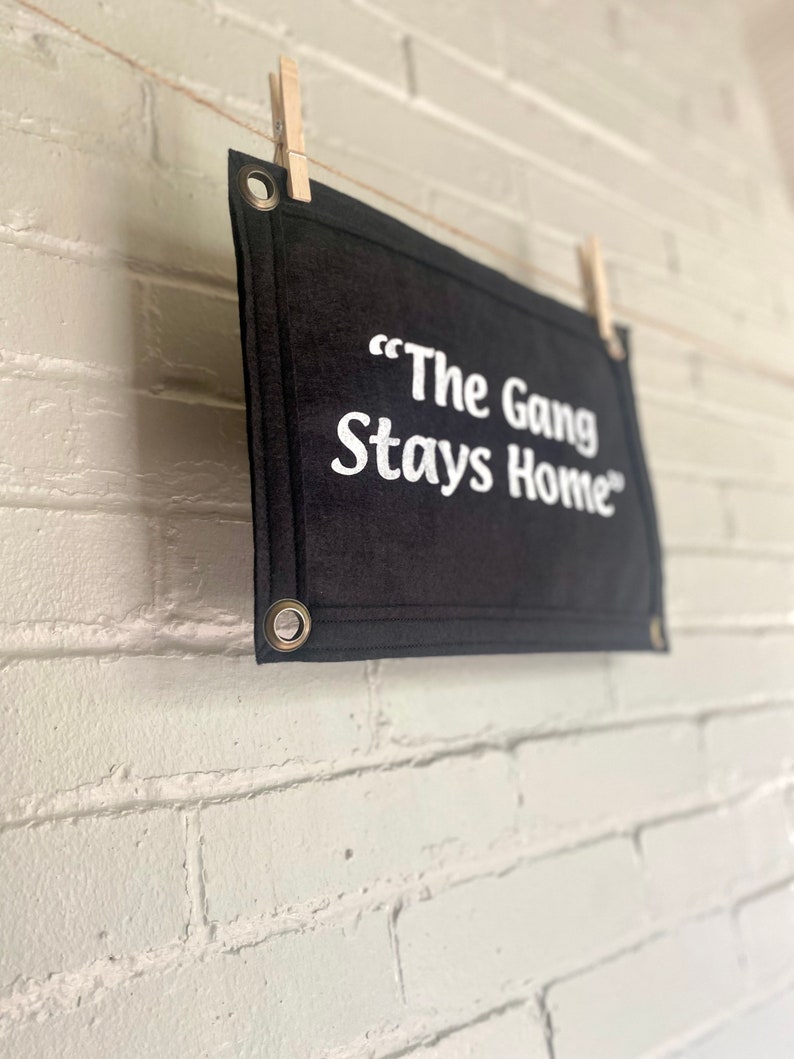 A black felt banner with a phrase in bright white ink reading "The Gang Stays Home" in the style of It's Always Sunny in Philadelphia.