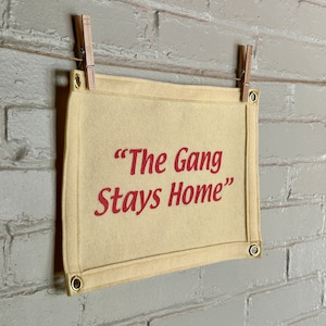 A cream felt banner with a phrase in bright pink ink reading "The Gang Stays Home" in the style of It's Always Sunny in Philadelphia.