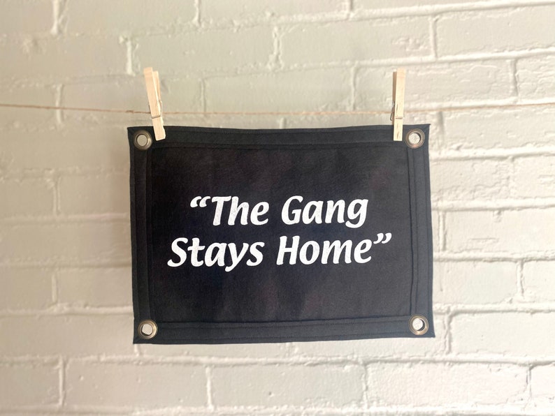 A black felt banner with a phrase in bright white ink reading "The Gang Stays Home" in the style of It's Always Sunny in Philadelphia.