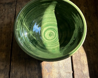 May include: A deep green ceramic bowl with a glazed finish. The bowl has a slightly rounded shape and a smooth, even surface.
