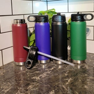 May include: Four stainless steel water bottles with different colored lids and bodies. The bottles are lined up in a row on a countertop. The colors are burgundy, blue, black, and green.