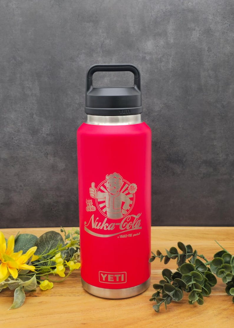 May include: Red YETI Rambler 36 oz. bottle with a black handle and lid. The bottle has a laser-etched design of a cartoon character with the text "Stay  Ice Cold" and "Nuka-Cola - A Vault-Tec product".