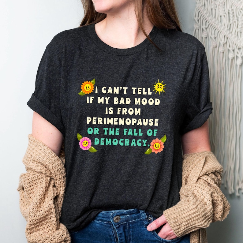 A funny and bold t-shirt featuring perimenopause humor and a political statement on the fall of democracy, designed for women who embrace activism with wit.