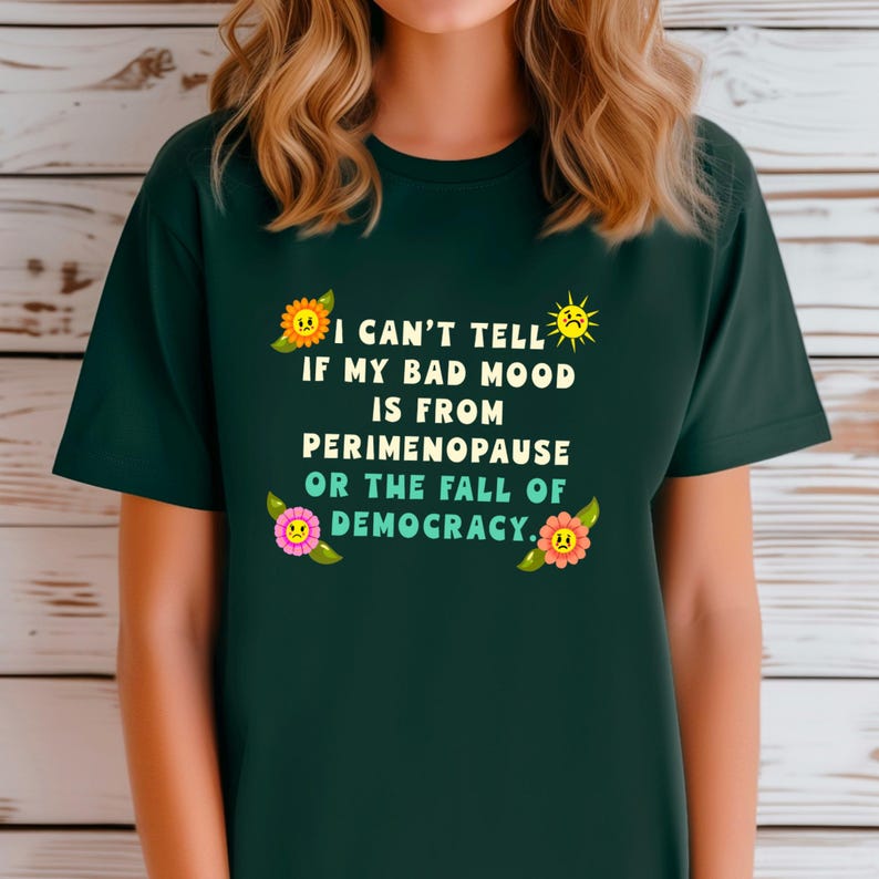 A funny and bold t-shirt featuring perimenopause humor and a political statement on the fall of democracy, designed for women who embrace activism with wit.