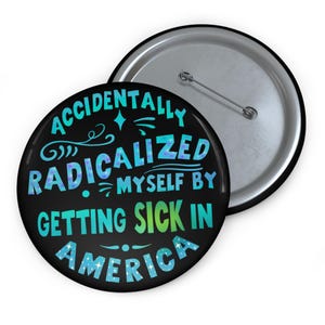 May include: A black button with the text "ACCIDENTALLY RADICALIZED MYSELF BY GETTING SICK IN AMERICA" in teal, blue, and green. The button has a silver pin back and is next to another button with a silver finish.