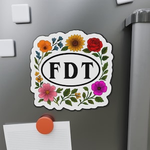 以下が含まれることがあります： カラフルな花輪で囲まれた、黒い文字で「FDT」と書かれた白い楕円形のステッカー。花には赤、黄、ピンク、紫、オレンジがあります。
