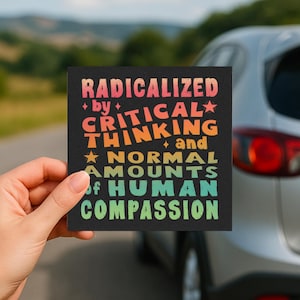 Pode incluir: Um autocolante quadrado preto com o texto "RADICALIZED by CRITICAL THINKING and NORMAL AMOUNTS of HUMAN COMPASSION" numa fonte retro colorida. O autocolante é segurado em frente de um carro.