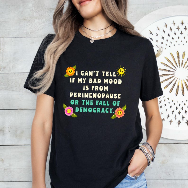 A funny and bold t-shirt featuring perimenopause humor and a political statement on the fall of democracy, designed for women who embrace activism with wit.