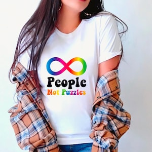 May include: White t-shirt featuring a rainbow infinity symbol and the text "People Not Puzzles" in black.