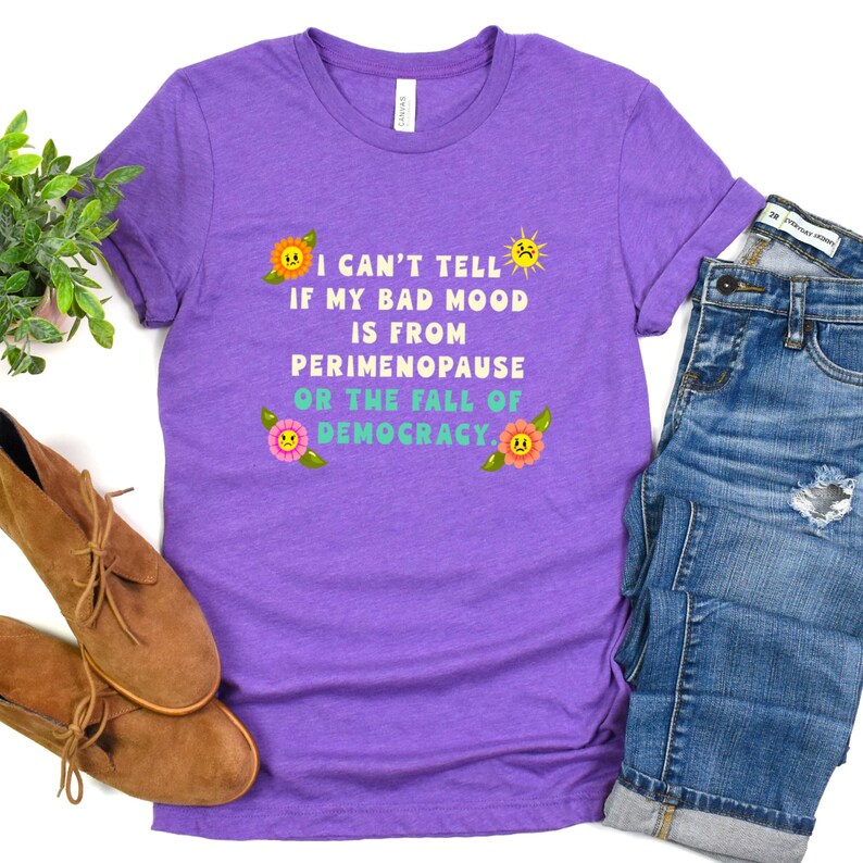 A funny and bold t-shirt featuring perimenopause humor and a political statement on the fall of democracy, designed for women who embrace activism with wit.