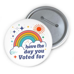 May include: A white button with a rainbow, sun, and stars. The text on the button reads "have the day you voted for".