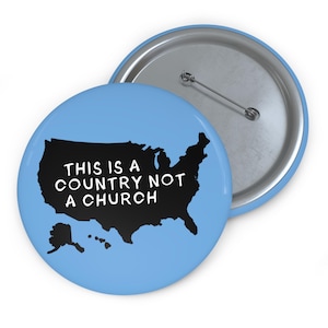 May include: A blue button with a black outline of the United States and the text "This is a country not a church" in white.