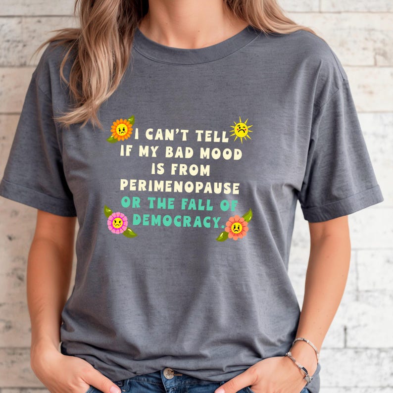 A funny and bold t-shirt featuring perimenopause humor and a political statement on the fall of democracy, designed for women who embrace activism with wit.