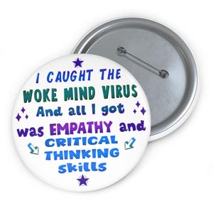 Può includere: Un bottone bianco con il testo "I CAUGHT THE WOKE MIND VIRUS And all I got was EMPATHY and CRITICAL THINKING skills" in blu, verde e viola. Il bottone ha un retro con spilla argentata.